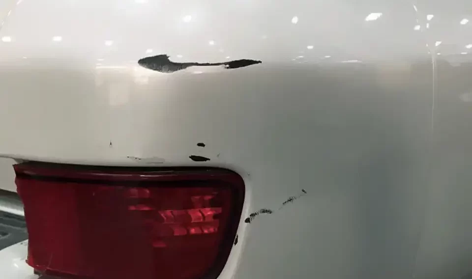 Closeup of a paint damage on a white car before repair.