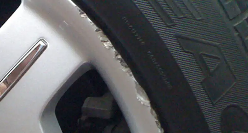 Closeup of a damaged painted alloy wheel before a repair.