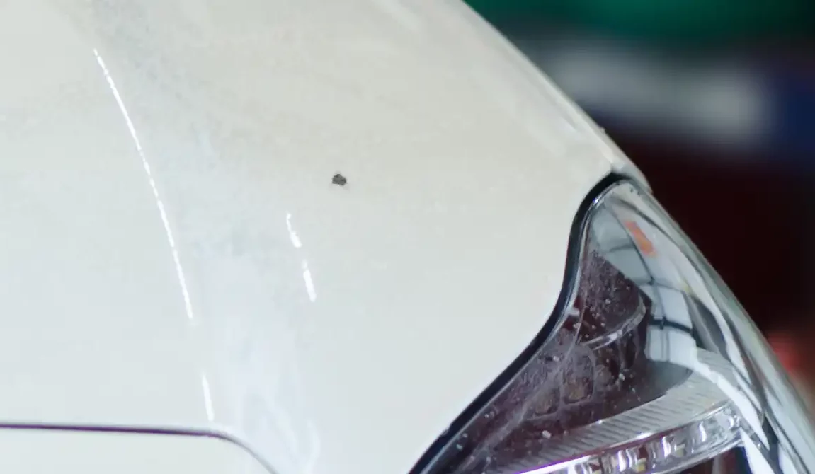 Closeup of a stone chip damage on a white car before repair.