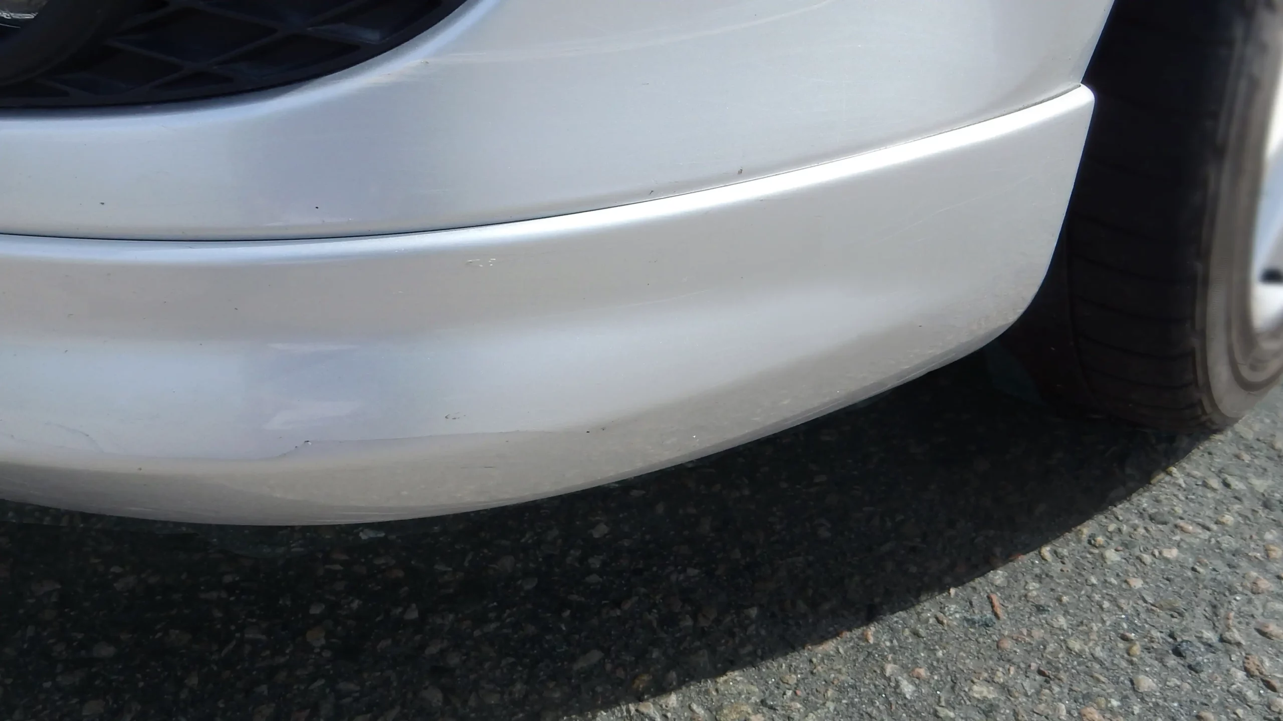 Nahaufnahme eines gebrochenen vorderen Stoßfängers an einem weißen Auto nach einer Kunststoffreparatur in der Werkstatt von Repair2Care.