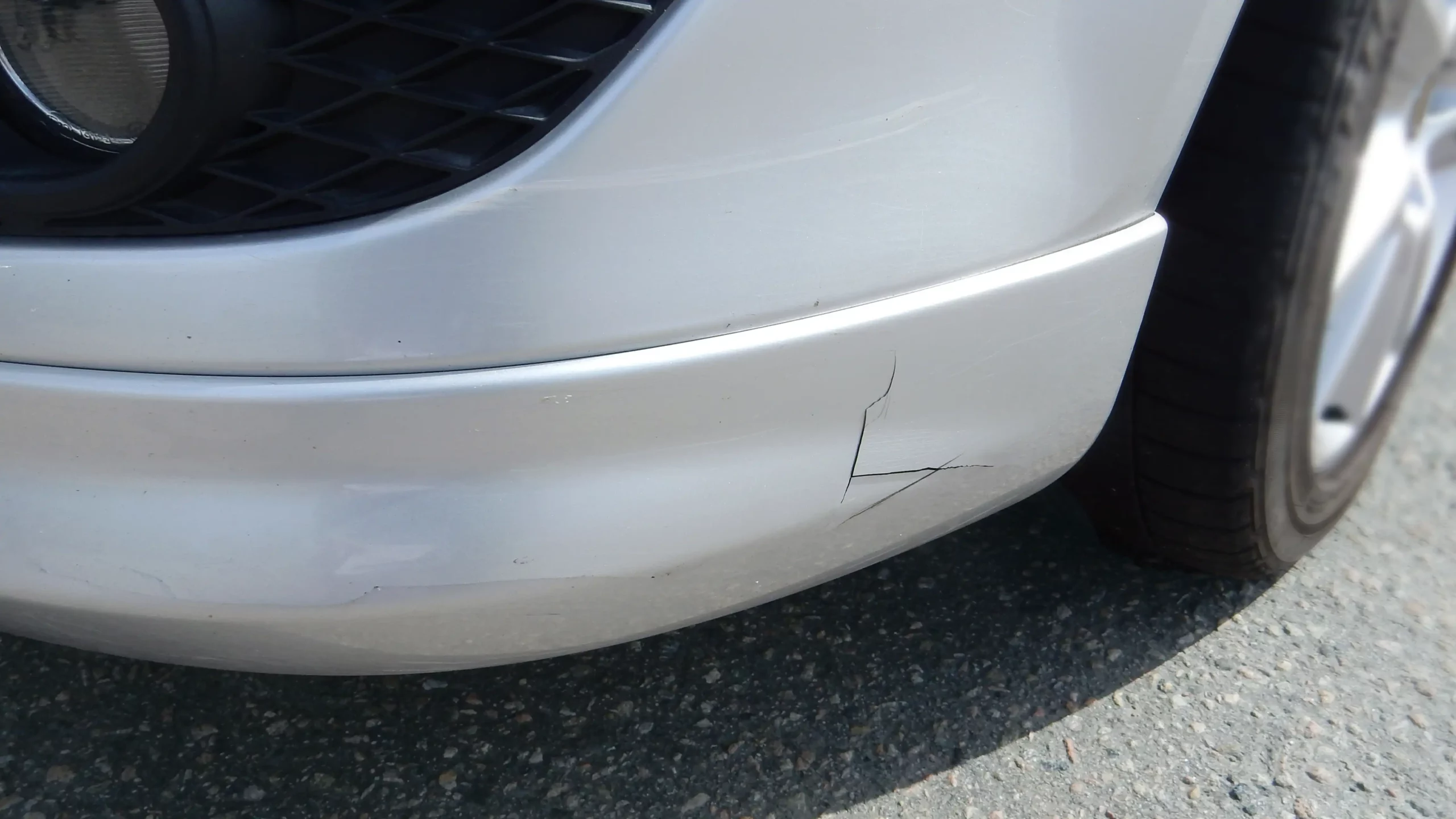 Nahaufnahme eines gebrochenen vorderen Stoßfängers an einem weißen Auto vor einer Kunststoffreparatur.