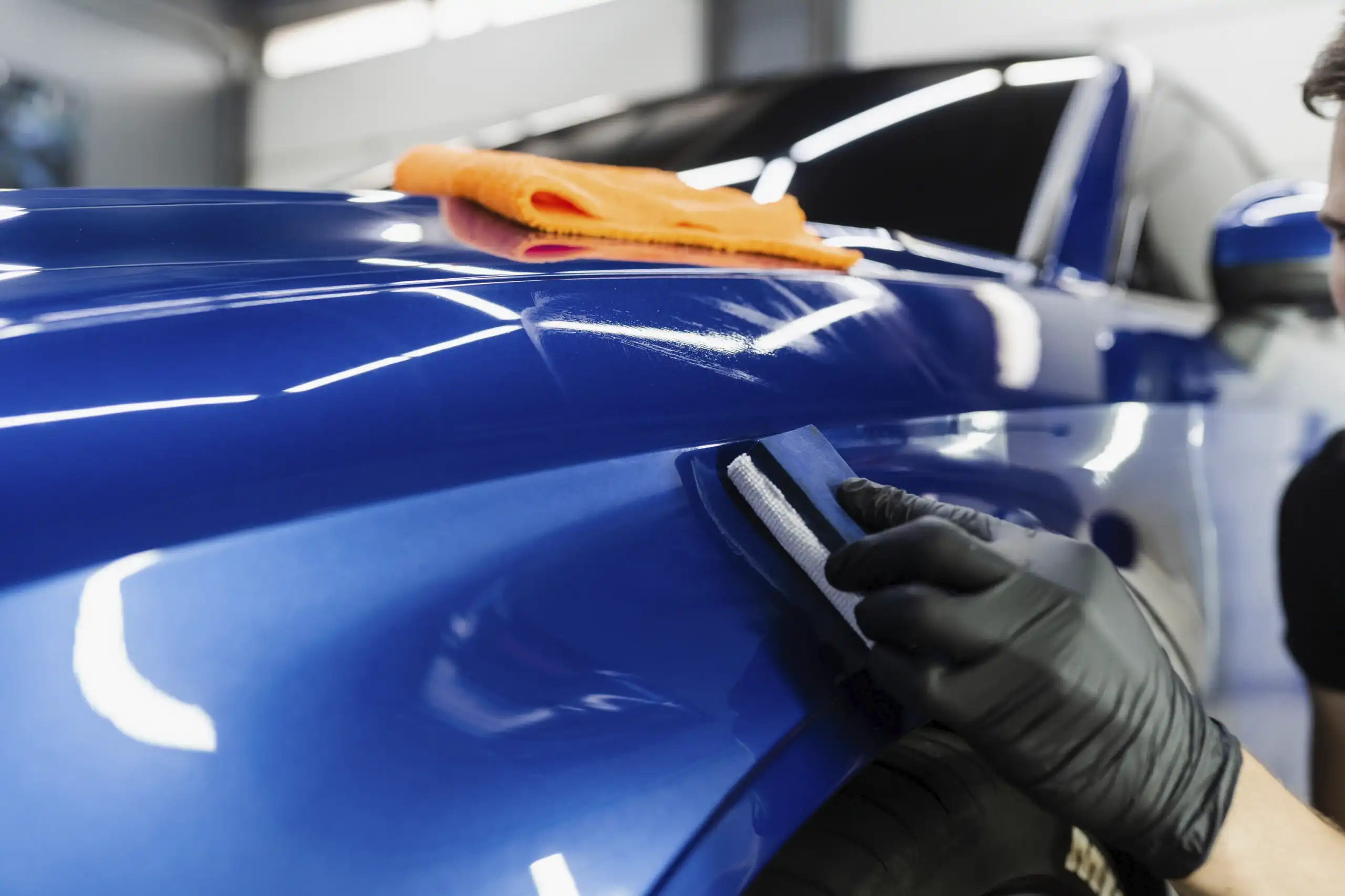 Closeup of technician applying a clear ceramic coating on a blue car.