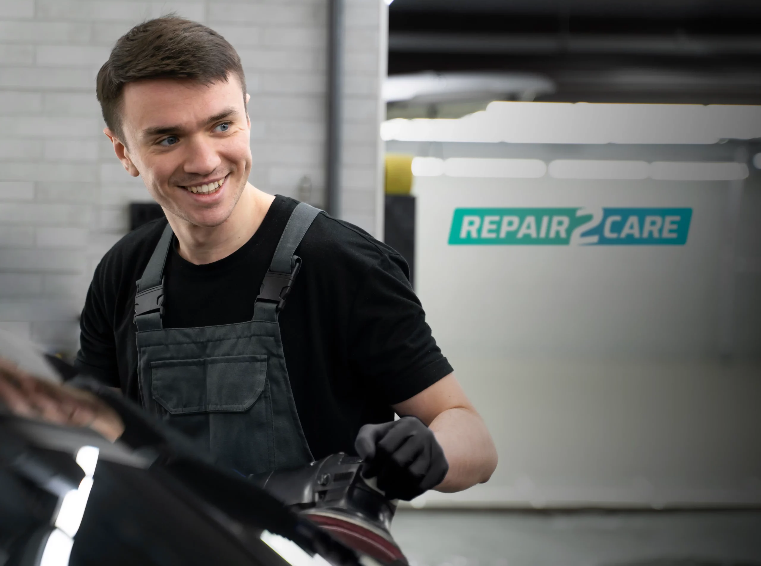 Technician smiling in workshop while polishing car.