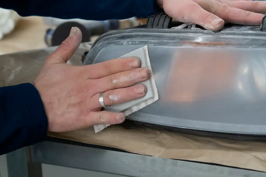 A technician sanding a mat headlight during a headlight repair and polish.