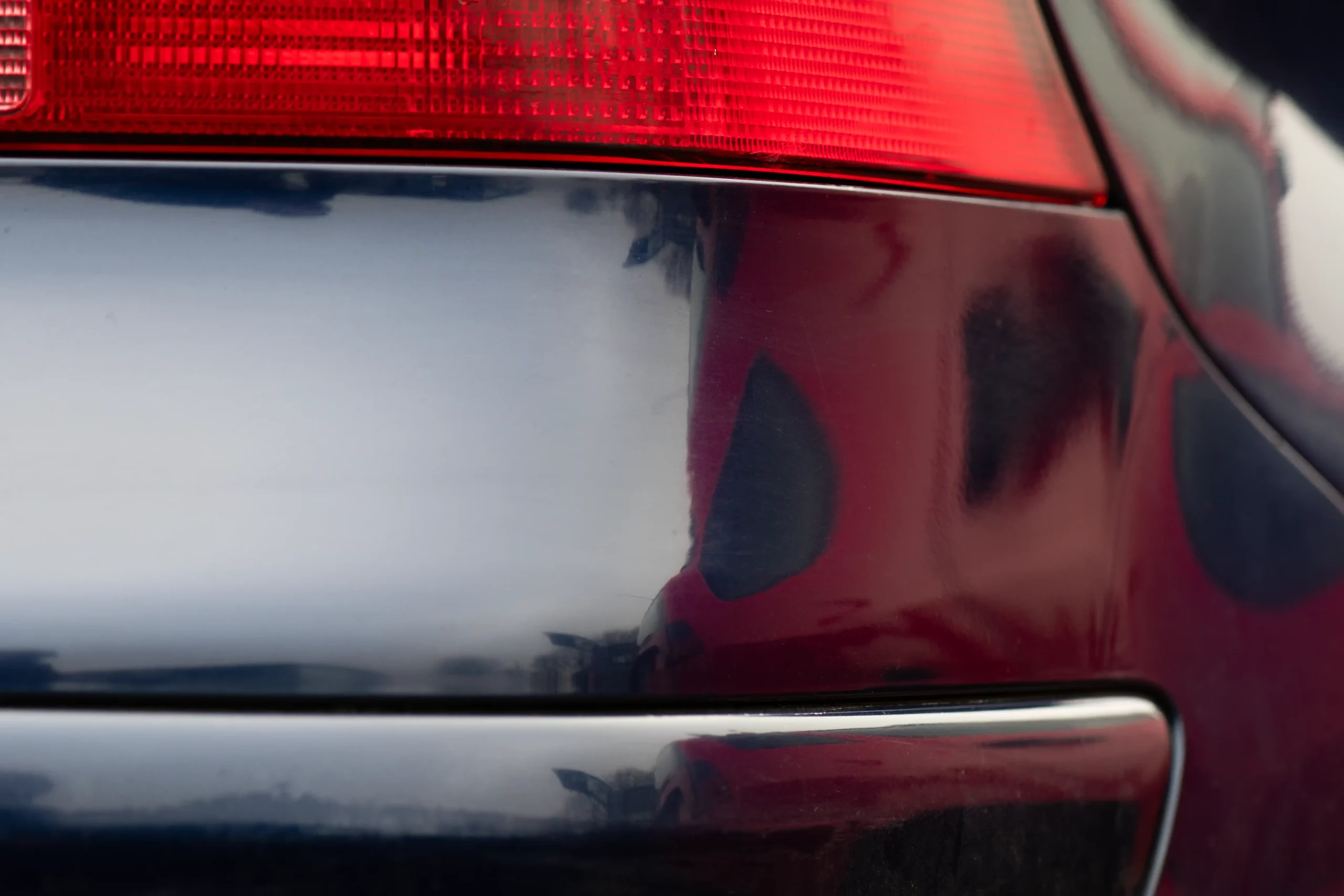 Efterbillede af en lakreparation på bagkofangeren af en mørkeblå bil.