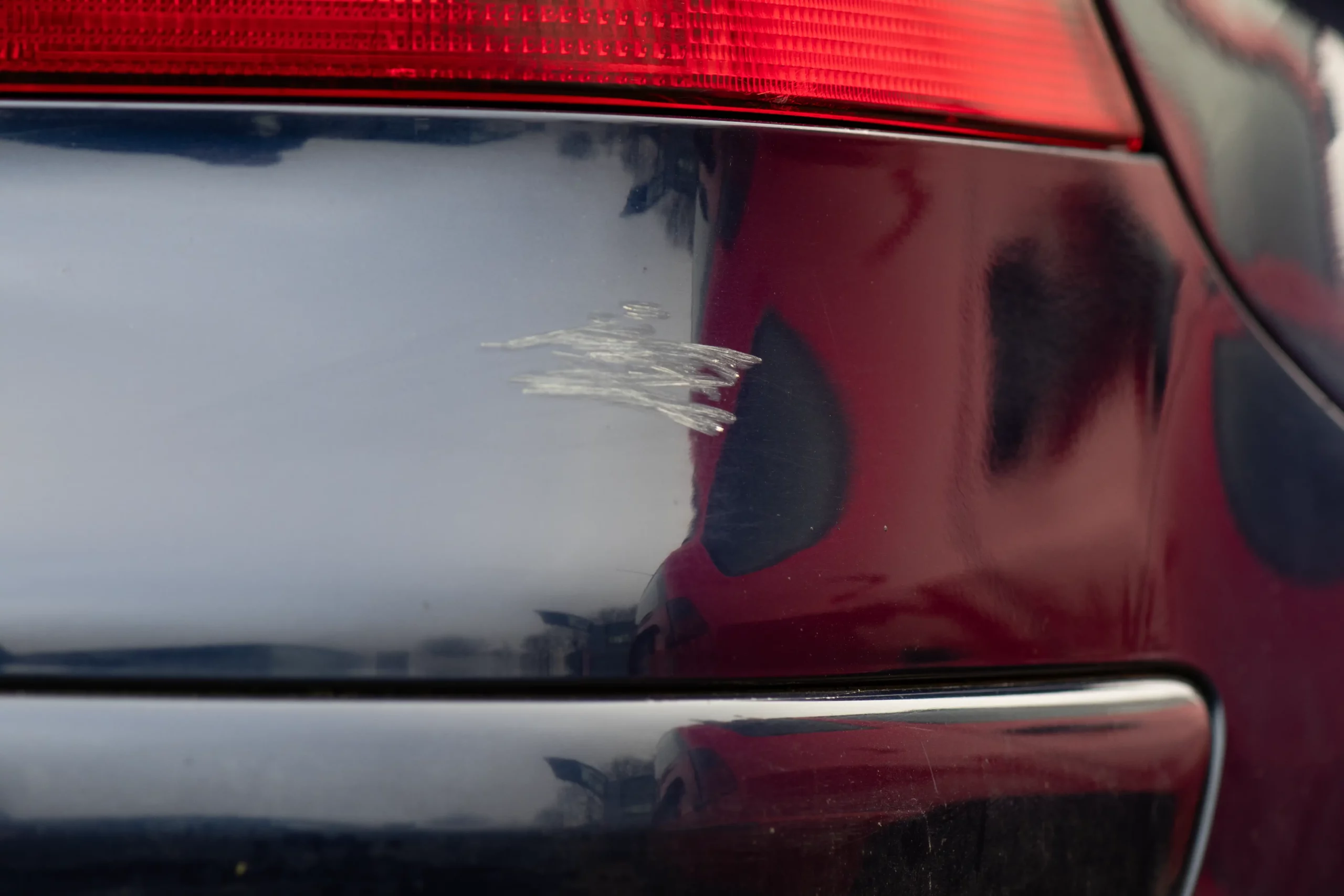 Das Vorher-Bild einer Lackreparatur an der hinteren Stoßstange eines dunkelblauen Autos.