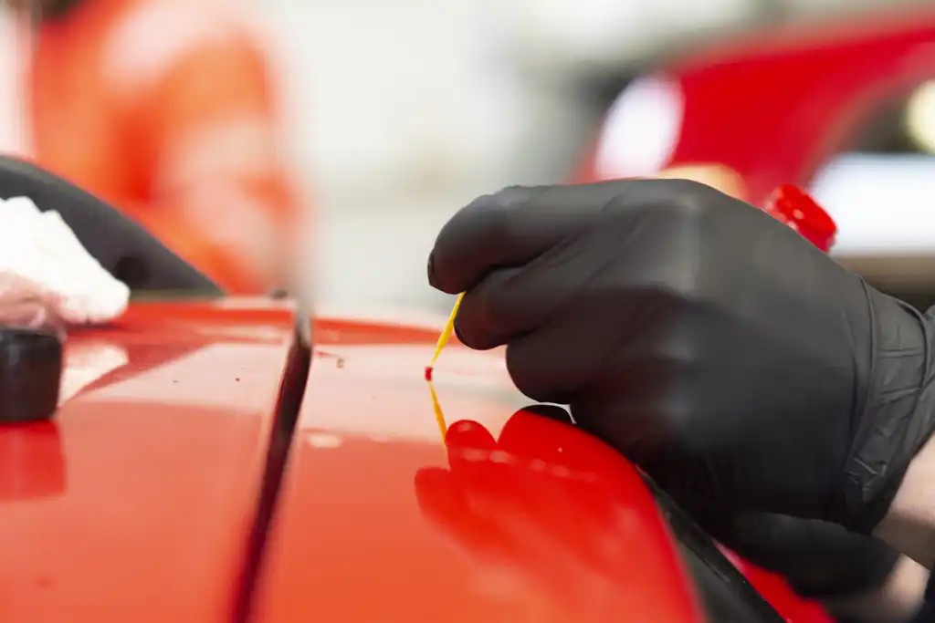 Techniker beim Ausbessern eines Lackflecks an einem glänzend roten Auto.