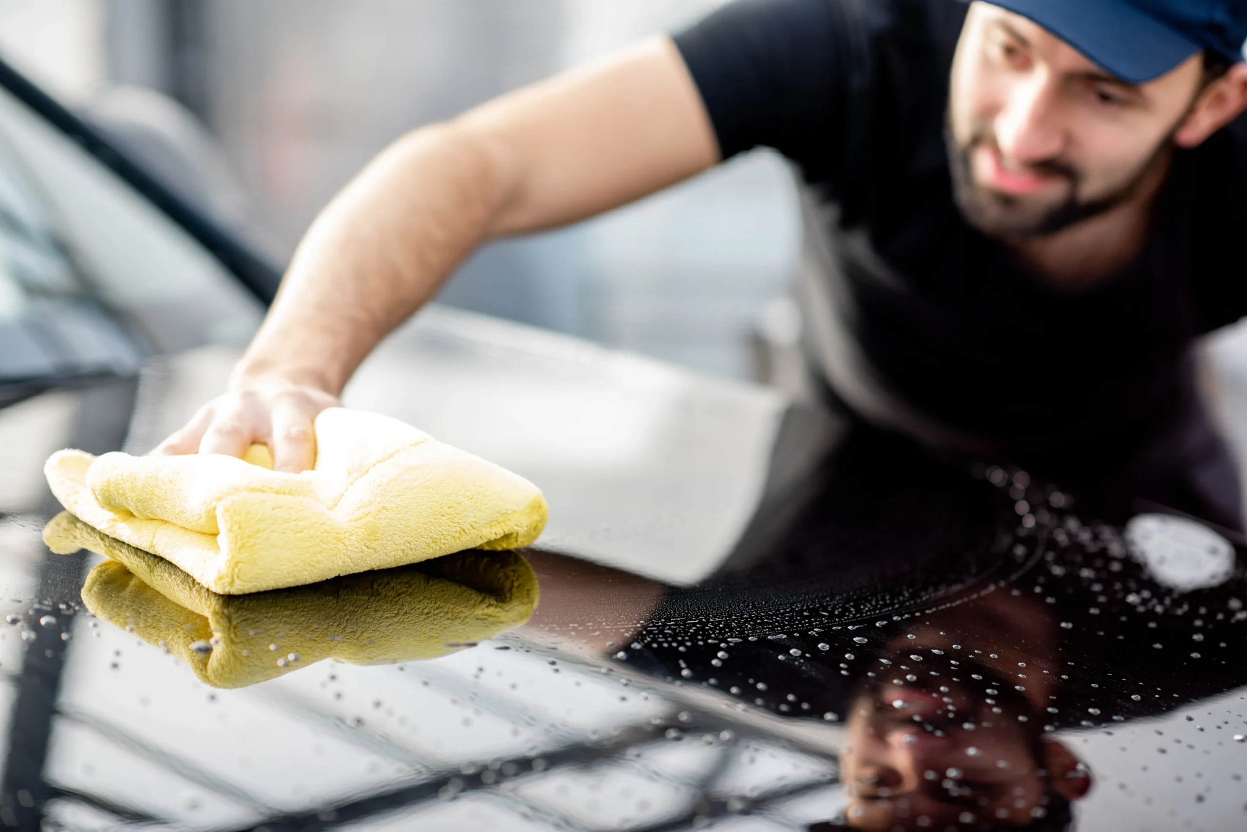 Professional washing the hood of a car with a microfiber cloth