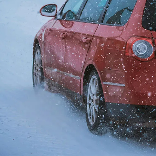Red car driving in the snow on winter tires