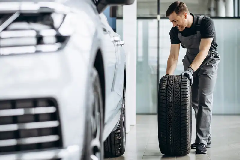 Smiling male technician walks with a tire in a car repair shop.
