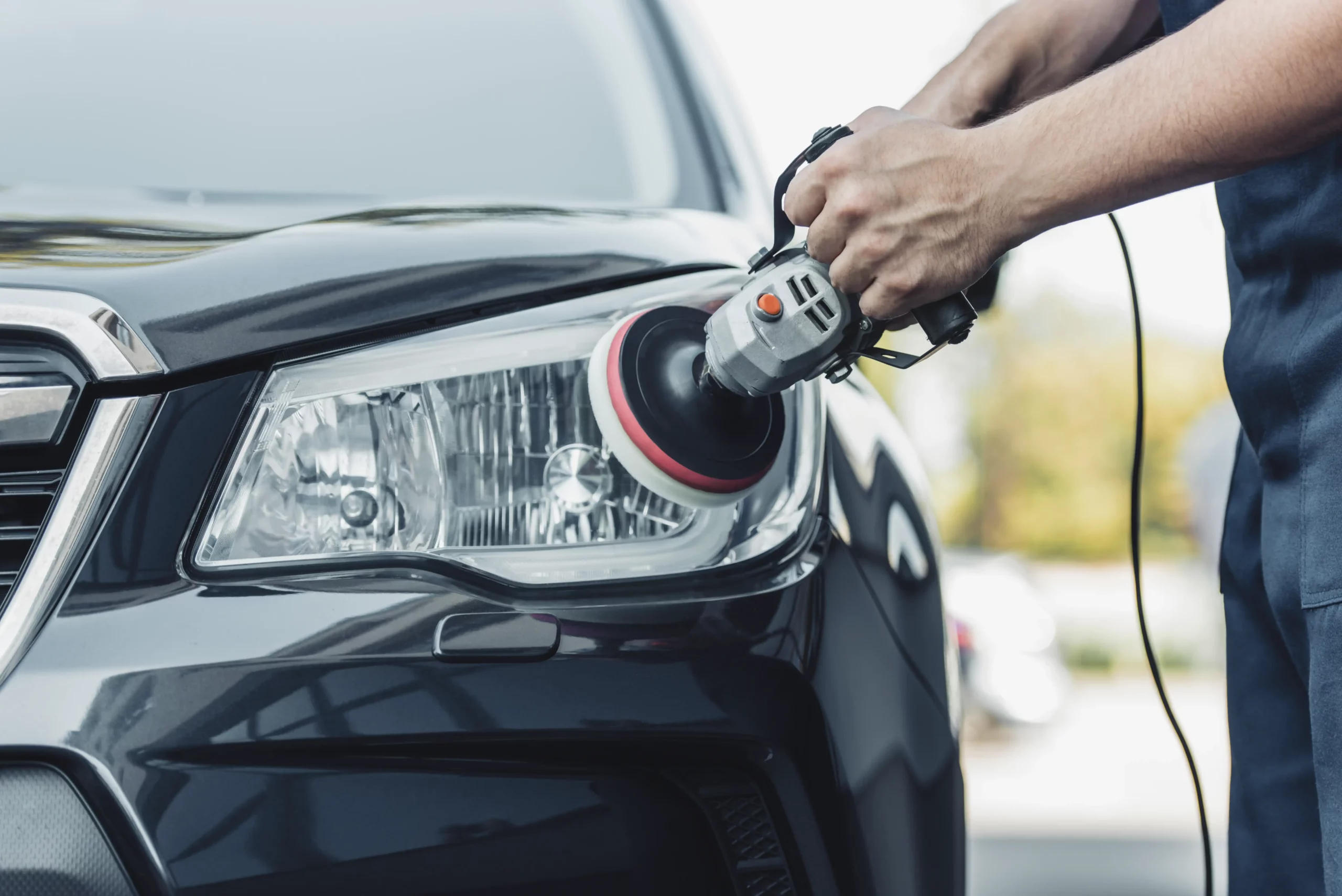 Technician polishing a car headlight on a black car.