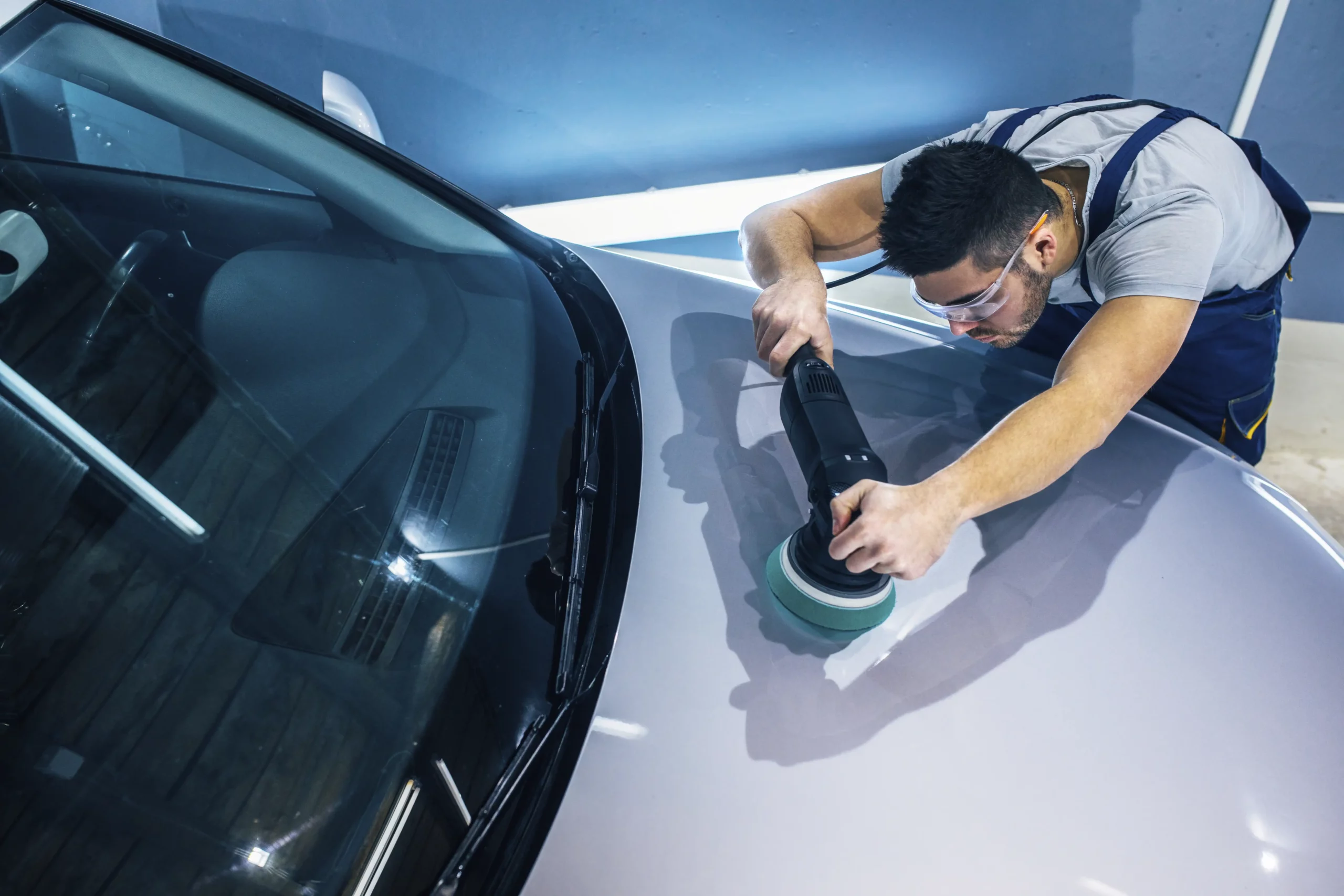 Technician polishing silver colored car in a workshop.