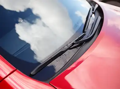 Forrude på rød bil med himlen reflekteret i vinduet.