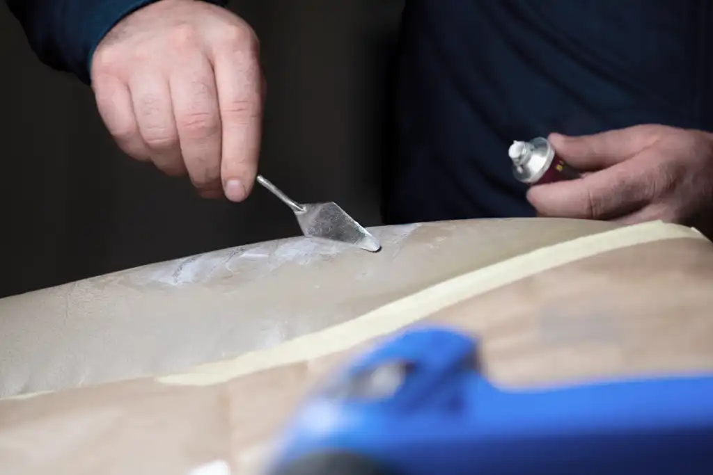 A technician is applying crack filler in a worn and cracked leather seat.