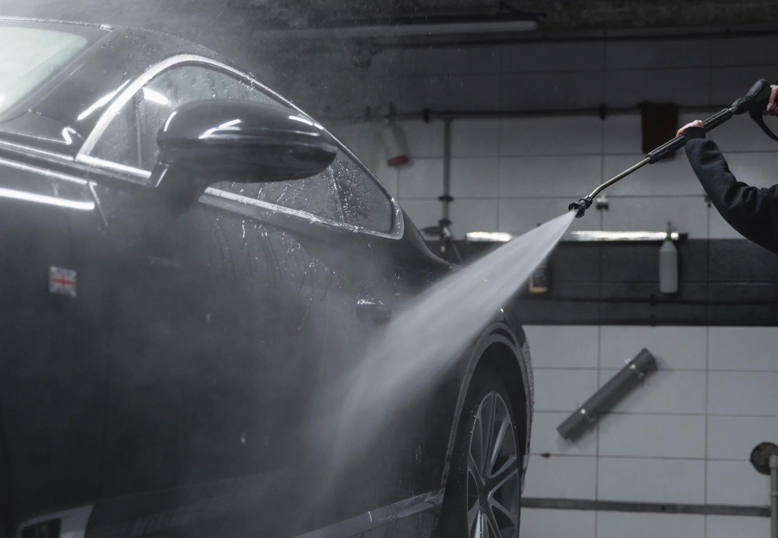 Technician using a high pressure washer to wash car in workshop.