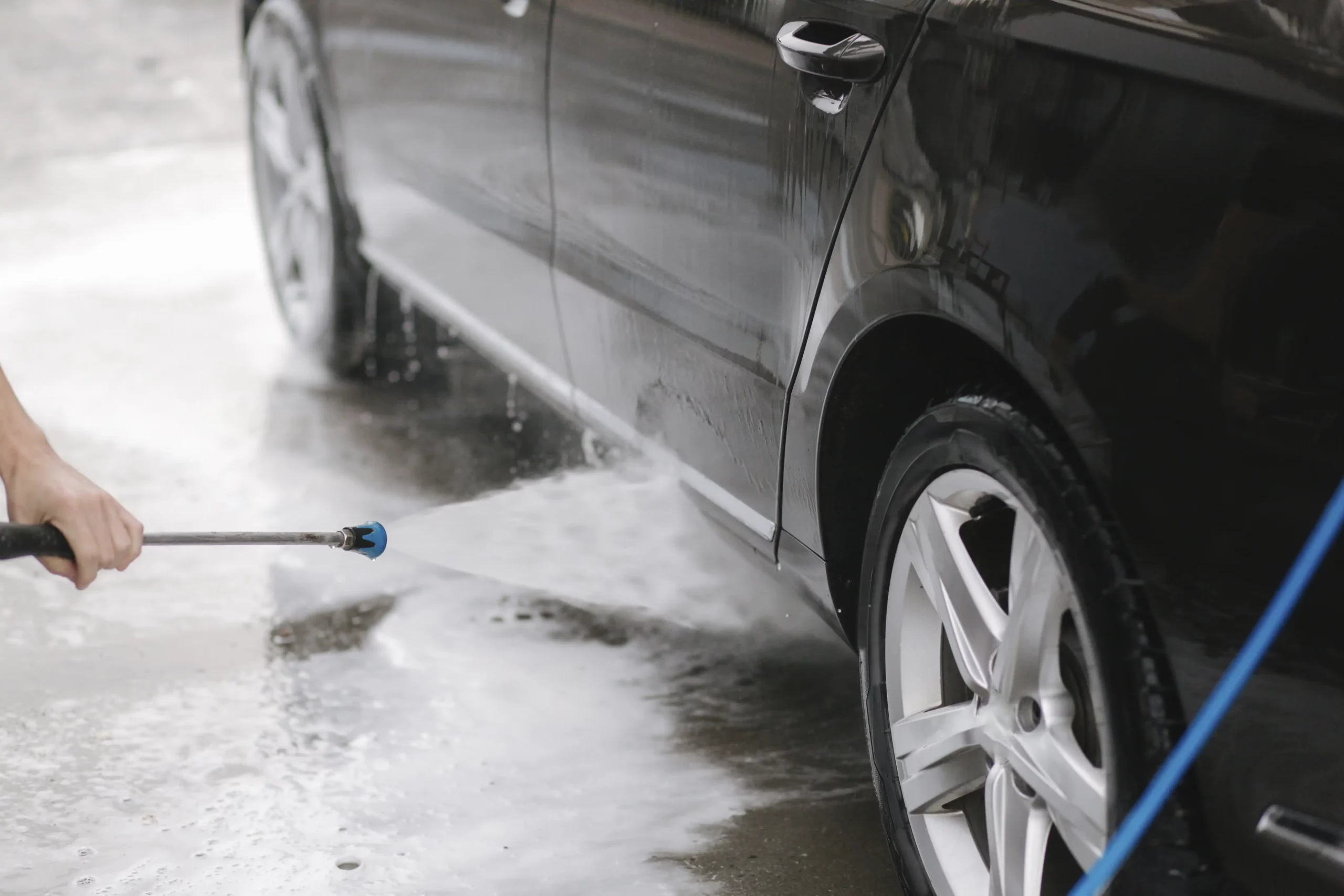 En tekniker tvättar en svart bil med en högtryckstvätt.